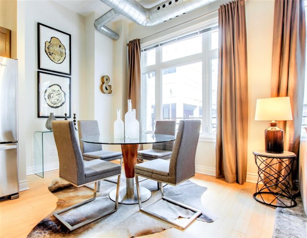 Starting as an empty canvas, this ground-floor condo, with its stark white walls, pale flooring, and visible cold metal ducts, presented a challenge in creating a warm, inviting atmosphere. The addition of noteworthy rental pieces (art, accessories, floor coverings, furniture) and the inclusion of opulent window treatments introduced a rich layer of color and warmth, dramatically enhancing the elegance of the space.